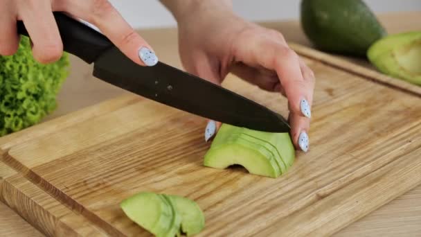 Vrouwenhanden snijden geschilde avocado op plakjes. Een avocado in stukken snijden. Gezond voedsel bereiden. — Stockvideo