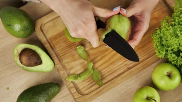 Le donne sbuccia e taglia kiwi. Avocado a fette kiwi e mele sul tavolo. tagli e bucce di kiwi fresco succoso per un'insalata di frutta. Dieta, poche calorie, vegetarianismo, vitamine naturali. — Video Stock