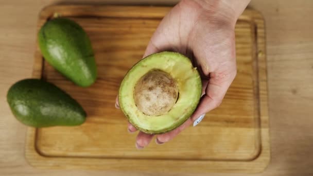 Veganistisch trendy eten. Vrouw met de helft van verse rijpe avocado in de hand, bovenaanzicht — Stockvideo