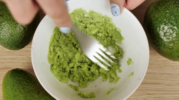 Handen vrouw verpletterende avocado in kom met een vork. Beelden van het tafelblad. Gezond koken — Stockvideo