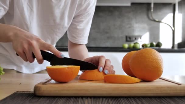 Chica cortando naranja en rodajas en un tablero de bambú en la cocina — Vídeos de Stock