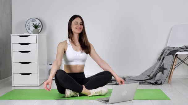 若い女性が自宅でオンラインヨガをやってリラックスして瞑想します。健康的なライフスタイルのコンセプト. — ストック動画