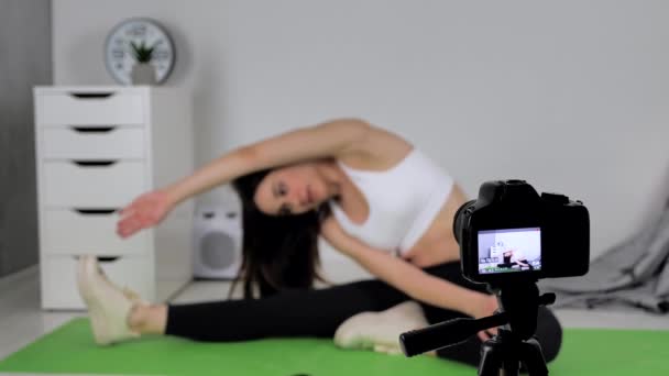 Mujer haciendo ejercicio, haciendo ejercicio de estiramiento en una esterilla de yoga y dispara vídeo en línea en la cámara en casa. Inclinación lateral — Vídeos de Stock