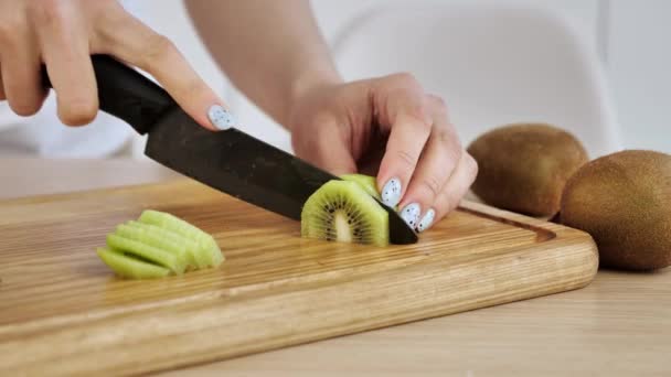 Kvinnan skar kiwi på en träskiva i köket. — Stockvideo