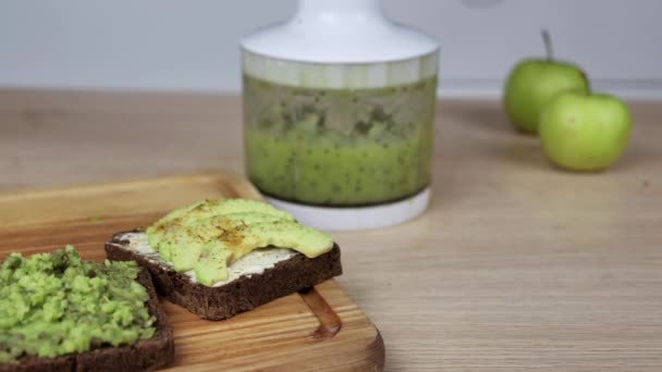 Rostat bröd med bitar avokado och guacomole på träskiva bakgrund. Hälsosam kost koncept. Grön färsk smoothie på bakgrunden — Stockvideo