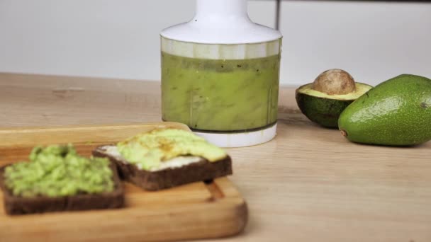 Vegansk mat i köket arbetsyta. Moderna trender inom hälsosam kost. Avokado skivor av med färskost på rostat bröd, kiwi smoothie i en mixer — Stockvideo