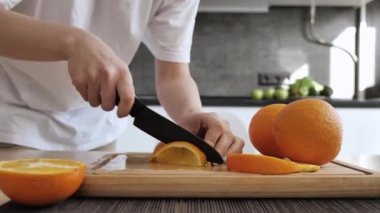 Kadın eli turuncu kesilmiş. Tahtada dilimlenmiş portakal, mutfak arka planında. Diyet, az kalori, vejetaryenlik, doğal vitaminler.