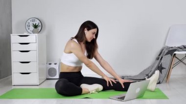 Çevrimiçi yoga öğrenen çekici, esnek bir kadın dizüstü bilgisayar, kablosuz kulaklık ve internet üzerinden ders izliyor.