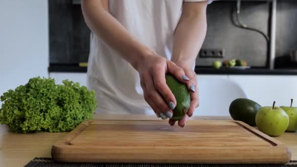 Закрыть женские руки держать две срезанные половинки свежего зеленого авокадо на кухне Фон. Вид спереди. Концепция здорового веганского питания — стоковое видео