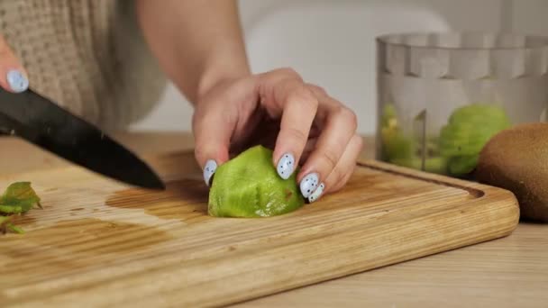 Concepto de desayuno saludable. Rebanando kiwi en trozos pequeños, con un cuchillo de cerámica, en una tabla de cortar de bambú — Vídeos de Stock
