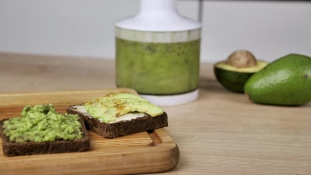 Vegansk mat i köket arbetsyta. Moderna trender inom hälsosam kost. Avokado skivor av med färskost på rostat bröd, kiwi smoothie i en mixer, matlagning smörgåsar — Stockvideo