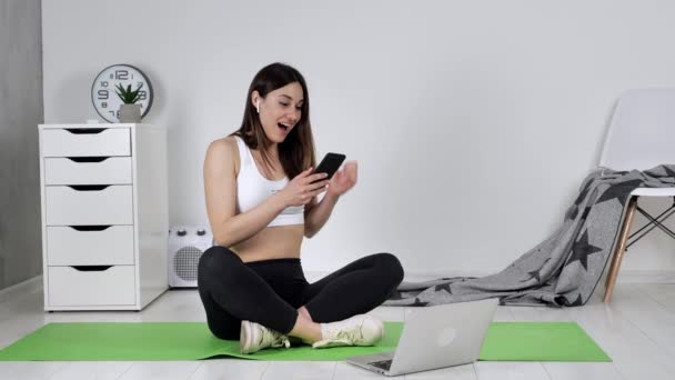 Frau sitzt auf dem Boden und hält Smartphone in der Hand, liest Nachrichten auf SMS und ist überglücklich, geballte Faust macht eine sehr glückliche Geste. — Stockvideo