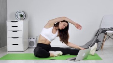Genç, formda bir kadın bilgisayarda esneme hareketleri dersi izliyor. Yan eğilme kavramı