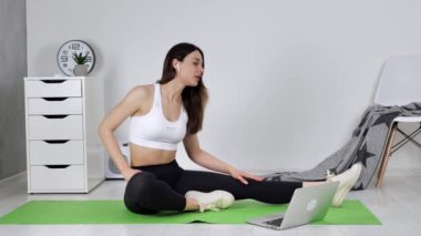 Mutlu bir kadın ev içi arka planda online antrenörle yoga yapıyor.