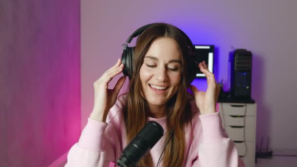 Uma jovem cantora profissional está executando uma nova música com um microfone enquanto a grava em um estúdio de música neon. — Vídeo de Stock
