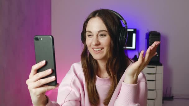 Mujer bonita de auriculares está haciendo videollamada en línea enviando beso de aire sonriendo charlando en casa solo. Concepto de personas y comunicación. — Vídeos de Stock