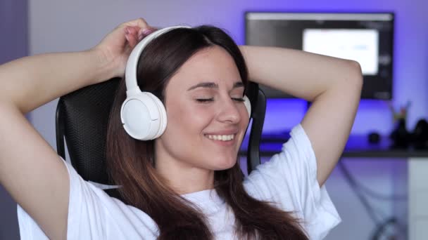 Disfrutar de la mujer el resto mientras está sentado en el sillón. Mujer joven escuchando música con auriculares inalámbricos — Vídeos de Stock