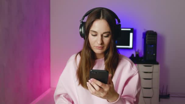 Een geschokte vrouw in een koptelefoon kijkt naar de camera met neon licht achtergrond — Stockvideo
