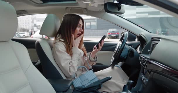 Una mujer joven se sorprende, desconcertada por lo que vio en un teléfono inteligente. Mujer sentada en coche. — Vídeo de stock