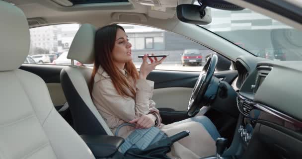 Mujer feliz millennial en abrigo beige activando asistente virtual en el teléfono móvil. Sonriente joven caucásica grabando contestando por mensaje de audio en red social para amigo o usando traductor — Vídeo de stock