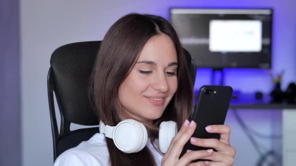 Mujer olorosa feliz en auriculares con teléfono inteligente en casa — Vídeos de Stock