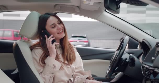 Giovane donna in cappotto beige che parla al telefono mentre è seduta in macchina — Video Stock