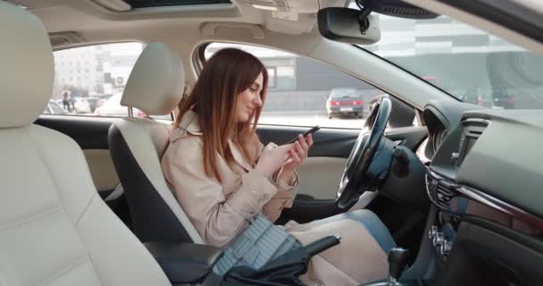 Lachende positieve brunette vrouw zitten in de auto het geven van opdrachten aan voice assistant, levende voice message of gewoon praten via luidspreker. — Stockvideo