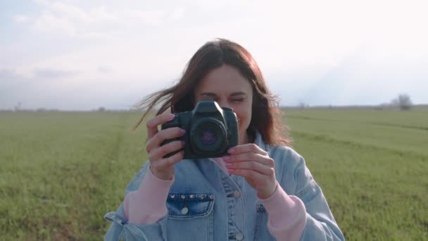 Красивая молодая женщина наслаждается фотографированием с камерой на свежем воздухе на зеленой лужайке. Вид спереди. — стоковое видео