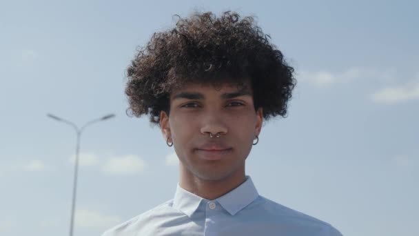 Portrait millennial african american on sky background. Lockiger Rüde dreht den Kopf zur Seite und lächelt mit den Zähnen. Aufrichtigkeit und gelebte Emotion — Stockvideo