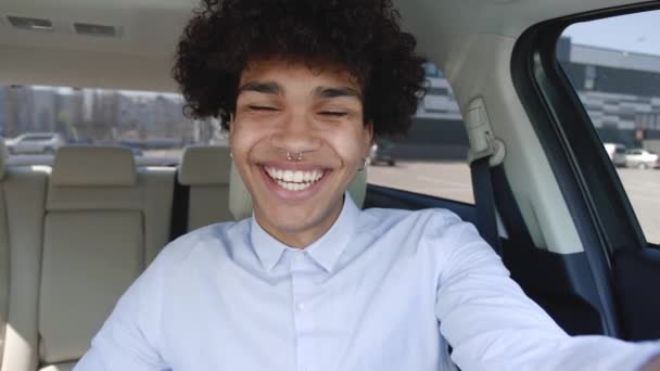 Вебкамера або відеофільм показує молодого афроамериканського студента-бізнесмена, який махає рукою, дивлячись на камеру і жестикулюючи сидячи в машині. — стокове відео