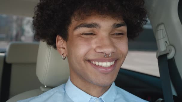Junger, lustiger afrikanischer Mann mit lockigem Haar, 20 Jahre alt, trägt ein blauweißes Hemd und posiert mit einem charmanten Lächeln im Auto. Menschen aufrichtige Emotionen Lifestyle-Konzept — Stockvideo