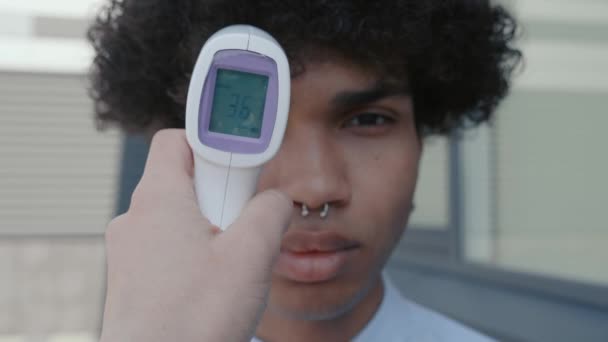 De hand drukt op de knop met behulp van elektronische thermometer en je kunt de temperatuur van Afrikaanse Amerikaanse, gezonde persoon te zien — Stockvideo