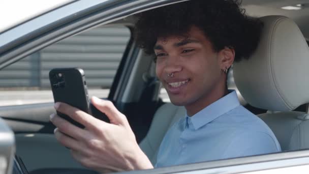 非洲裔美国学生正在使用智能手机，坐在汽车上，在社交网络上交流，男性小工具使用者。年轻人在打字 — 图库视频影像