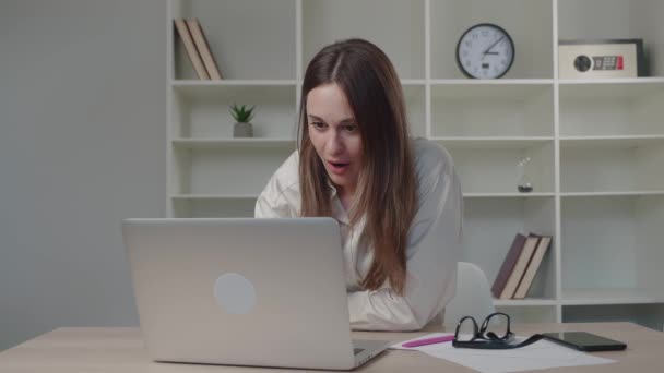 Mutlu bir milenyum kadını iyi haberler okuyan bir mesaj alıyor. Ofiste dizüstü bilgisayara bakarak başarıyı kutlayan aşırı mutlu bayan kazananımız. Laptop zafer konsepti — Stok video