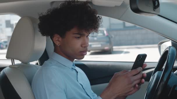 Πορτρέτο του μαύρου άντρα περιήγηση smartphone κάθεται ένα αυτοκίνητο ηλιόλουστη μέρα στο πάρκινγκ — Αρχείο Βίντεο