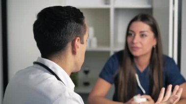 Masada oturan koyu mavi ceketli ciddi odaklı kadın doktor hastalık ya da ameliyat konusunda erkek doktora danışıyor. Dikiz manzaralı genç adam, genç doktorun konuşmasını dinliyor. Doktorlar danışır