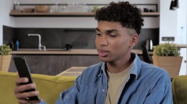 Gülümseyen Afro-Amerikan milenyumu akıllı telefonuyla 4K 'da video görüşmesi yapıyor.