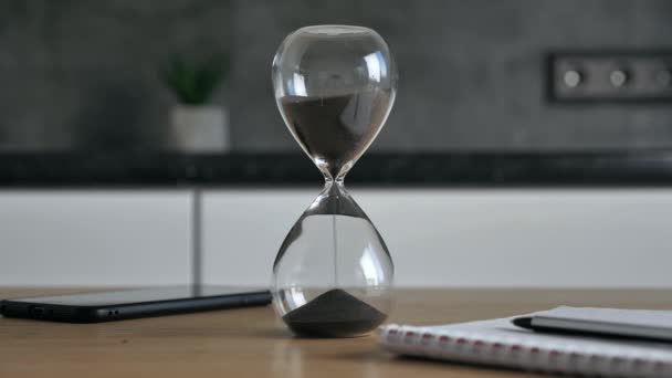 Tournage d'une horloge de sable mesurant le temps pendant que le sable tombe sur le sable noir sur fond de cadran flou. Ancienne minuterie classique. Concept de temps 4k — Video