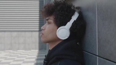 Kulaklıklı mutsuz bir Afro-Amerikan turist dışarıda müzik dinleyip sokakta akıllı telefon tutarak eğleniyor. Gençlik kültürü ve cihazları kavramı.