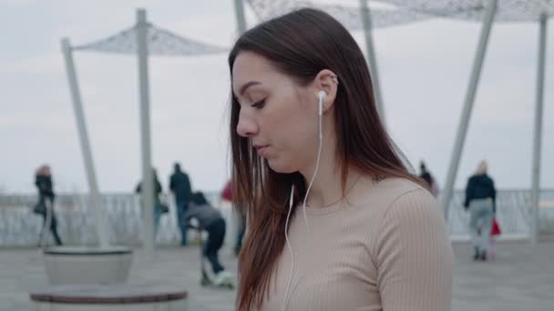 Кавказька вродлива жінка в навушниках сидить на терасі і слухає музику на вулиці. Одинока жінка задумлива, насолоджуючись піснями в місті. Знятий портрет. Концепція дозвілля — стокове відео