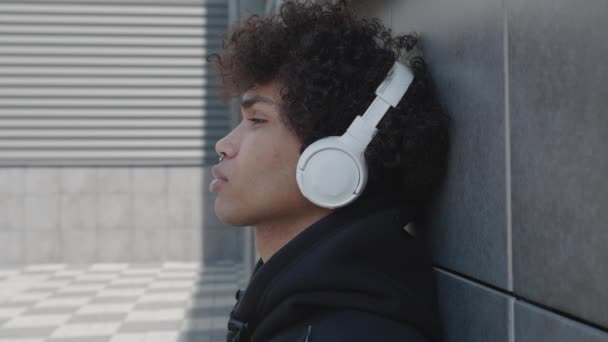 Turista afro-americano infeliz en auriculares escuchando música al aire libre divirtiéndose solo en la calle sosteniendo teléfono inteligente. Concepto de cultura y dispositivos juveniles. — Vídeo de stock