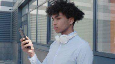 Kulaklıklı Afro-Amerikan turist dışarıda müzik dinleyip sokakta akıllı telefon tutarak eğleniyor. Gençlik kültürü ve cihazları kavramı.