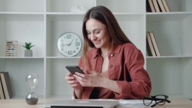 Telefon mesajı, büyüleyici gülüşlü mutlu genç bayan akıllı telefonu tut. Konsept sörf interneti, modern ofiste haberleri okumak