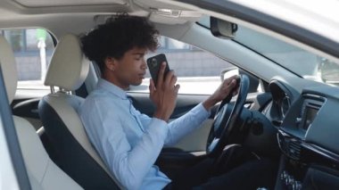 Yakın plan Afro-Amerikan adam. Arabadan telefona bakıyor. İyi giyimli adam arabada akıllı telefondan konuşuyor.
