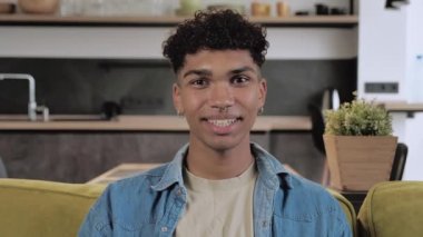 Orta boy, kendine güvenen Afrikalı Amerikalı yaratıcı adam vlogger canlı video konferans görüşmesi yapıyor, bilgisayarda sohbet ediyor ve evdeki koltukta oturuyor, webcam görüntüsü, görüntülü sohbet ve kişisel izolasyon kavramı..