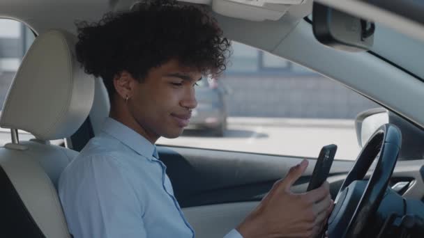 Bonito afro-americano sentado no carro para uma reunião importante e digitando em seu celular. Motorista procurando — Vídeo de Stock