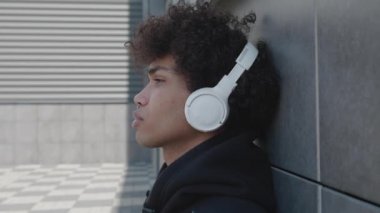 Kulaklıklı mutsuz bir Afro-Amerikan turist dışarıda müzik dinleyip sokakta akıllı telefon tutarak eğleniyor. Gençlik kültürü ve cihazları kavramı.