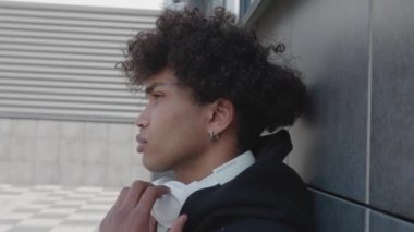 Binanın duvarına yaslanmış kulaklıklarla müzik dinleyen rahat Afro-Amerikan genç adamın videosu.