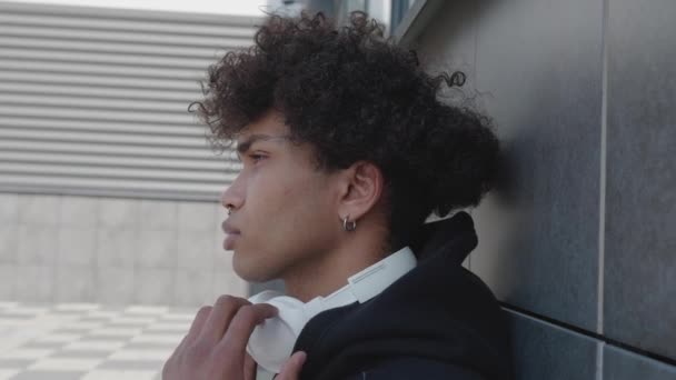 Video di un giovane afro-americano rilassato che ascolta musica con le cuffie appoggiate al muro di pietra dell'edificio — Video Stock