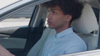 Gülümseyen Afro-Amerikan takım elbiseli adam araba sürüyor ve kameraya bakıyor.